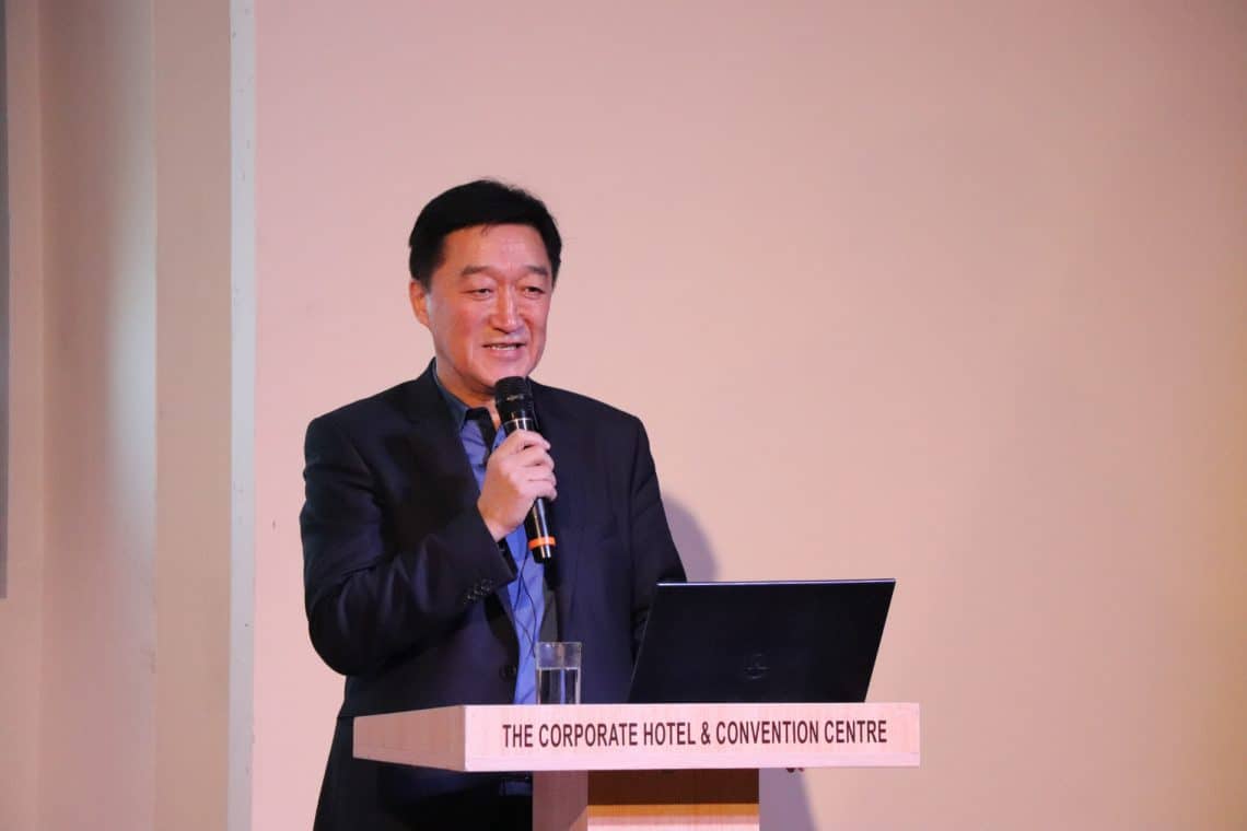 Костюм өмссөн эр "The Corporate Hotel & Convention Centre" гэсэн шошготой индэр дээр микрофоноор ярьж байна. - Business.MN