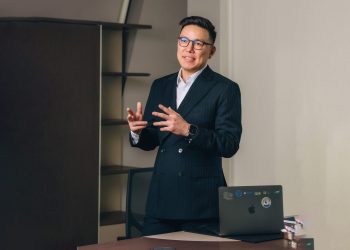 Харанхуй костюм, нүдний шил зүүсэн хүн зөөврийн компьютертэй ширээний ард зогсож, амжилттай энтрепренерийг бага зэрэг хардаг. Ярьж байхдаа гараараа дохио зангаагаар тэд өөртөө итгэлтэй байдаг. Ширээний хажуу талдаа цөөн хэдэн ном, ард нь хоосон тавиур байх нь оффисыг зохион байгуулалттай болгож байна. - Business.MN