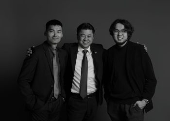 Албан ёсны ажил хэрэгч хувцас өмссөн гурван эрэгтэй инээмсэглэн зогсоно. Голд байгаа хүн нөгөө хоёрыг нь тэвэрчихсэн. Бүгд бизнесийн амжилттай удирдагчдын нэгдмэл байдал, мэргэжлийн ур чадварыг харуулсан харанхуй, энгийн дэвсгэр дээр байрладаг. - Business.MN