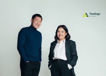 Саарал пиджак, цагаан цамц, хар өмд өмссөн инээмсэглэж буй эмэгтэйн хажууд цэнхэр хүзүүвч, хар өмд өмссөн инээмсэглэсэн эр зогсож байна. Тэд баруун дээд буланд Treelings лого, "Ургуулж үлдээе" гэсэн уриа бүхий цайвар дэвсгэр дээр зургаа авахуулж байна. - Business.MN