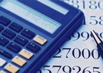 A blue calculator and a pen resting on a sheet filled with large printed numbers. The calculator display is visible, and the pen is positioned alongside, suggesting an active use of both tools for calculations or analysis.